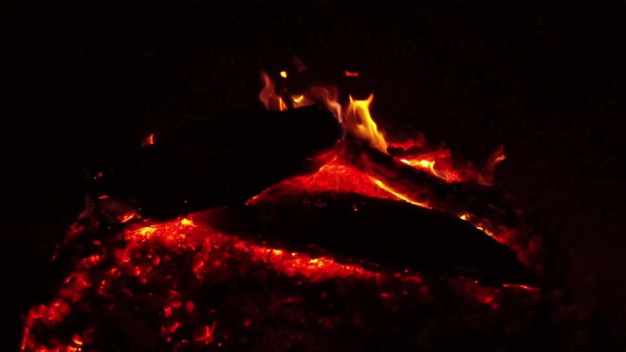 At 0:01, red coals glow across the lower frame while a charred log spans the middle and small flames rise from the upper log in Ojai, California, with no visible people.