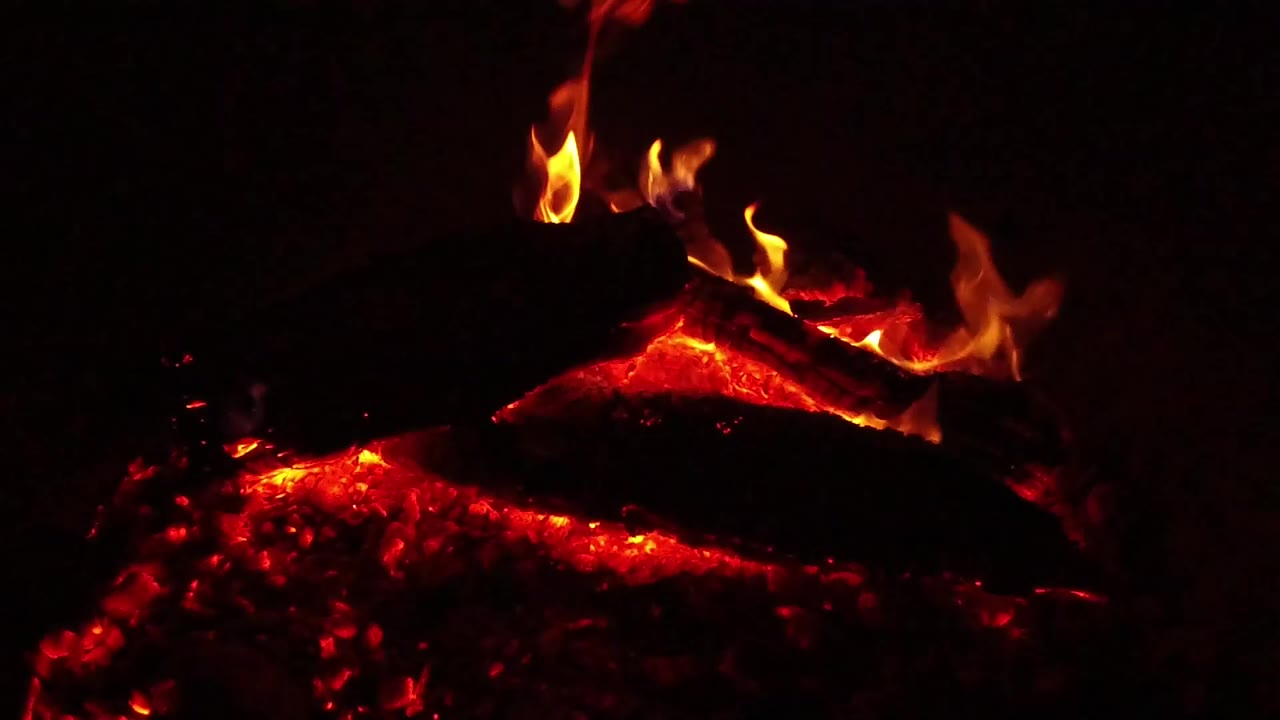 Close view of red burning wood and orange flames against a black background in Ojai, California, with no visible people.