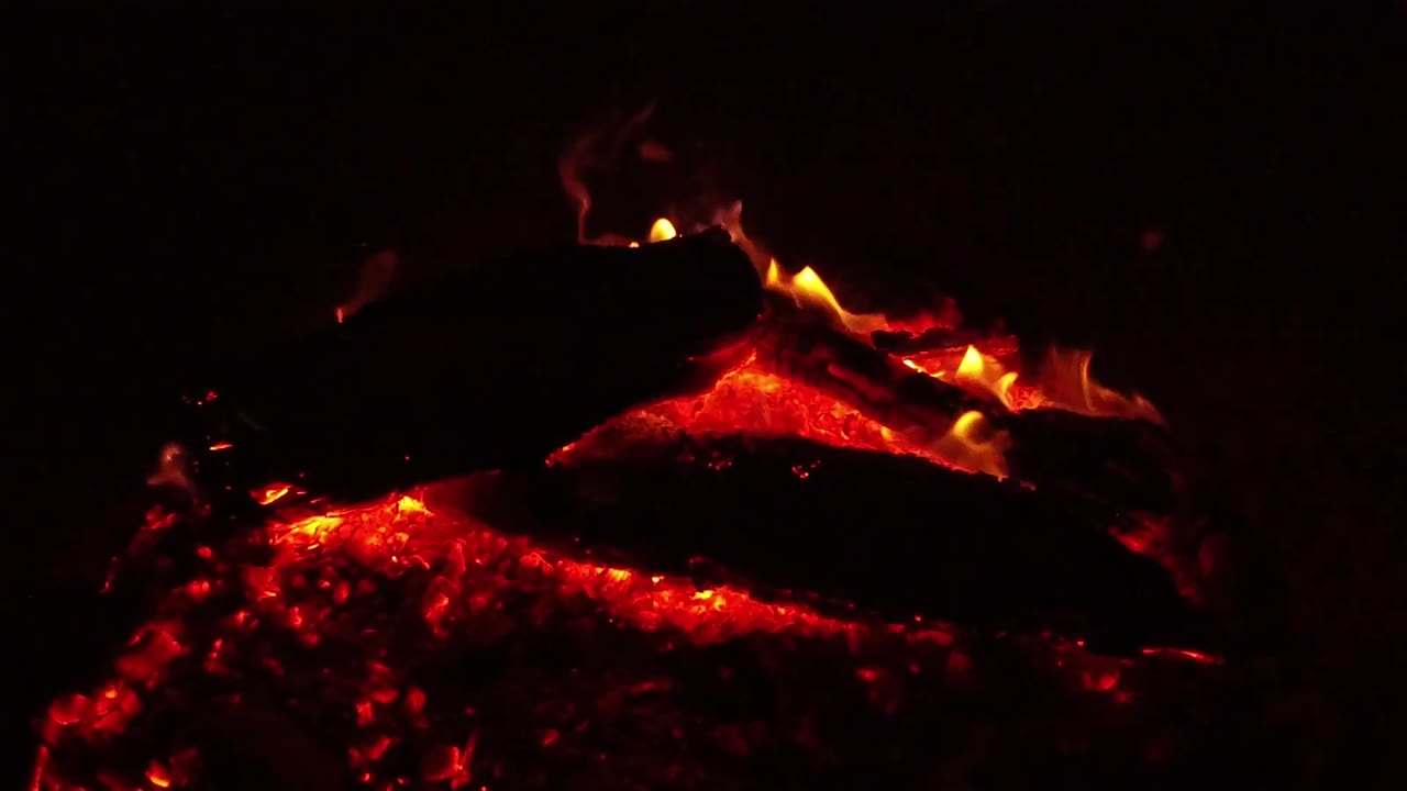A blackened log sits over red embers with small orange flames along its rim in Ojai, California, and no visible people.
