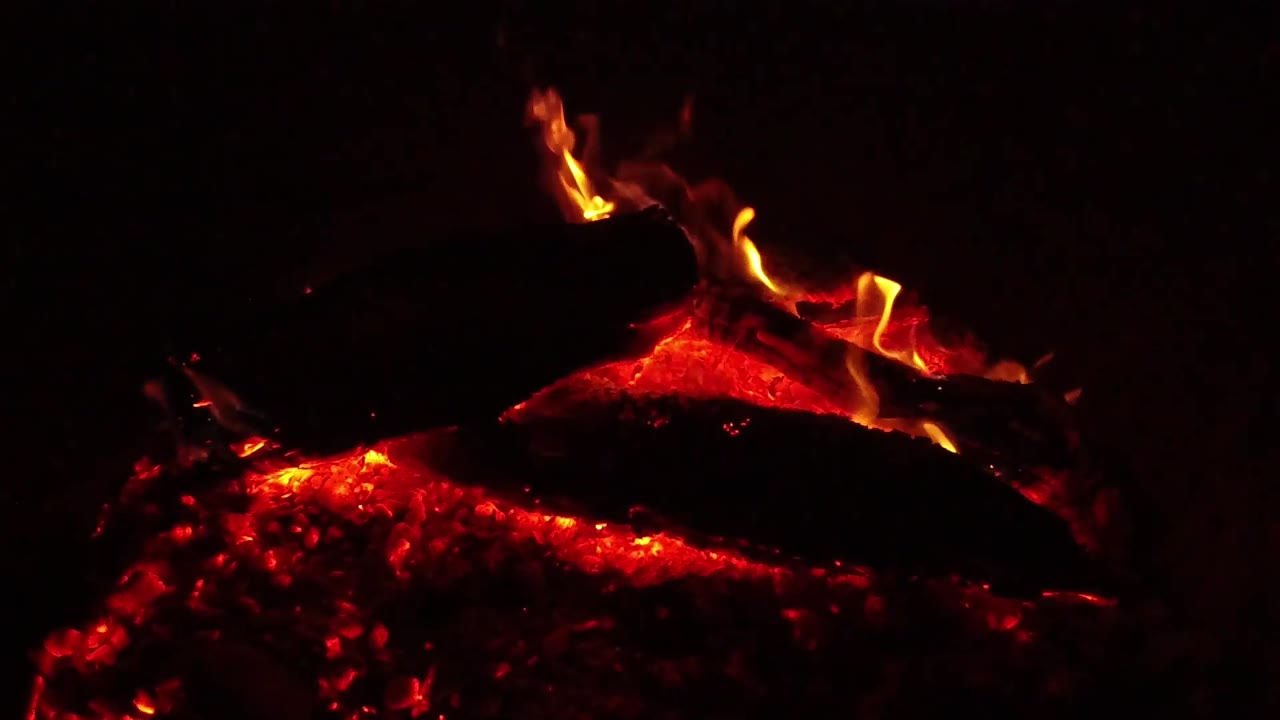 Red coals glow under a dark piece of wood as flame curls near the left and center edges in the Ojai, California clip, with no visible people.