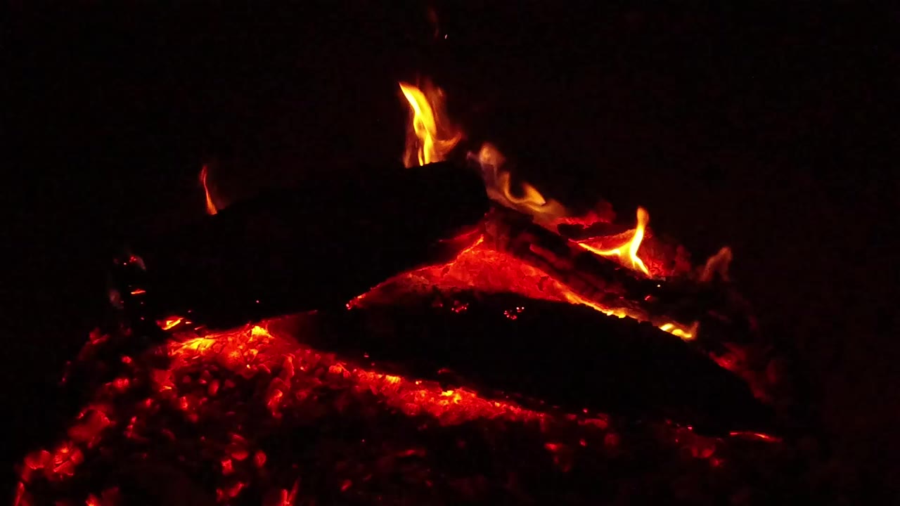 Orange flames rise from charred logs above glowing coals.