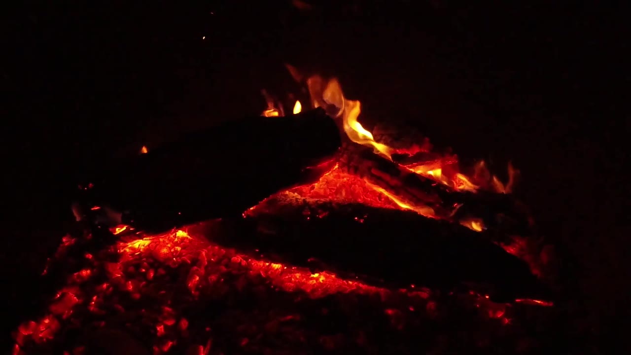 In the Ojai, California fire detail, low flames run along the upper log while red coals glow beneath a darker foreground log, with no visible people.