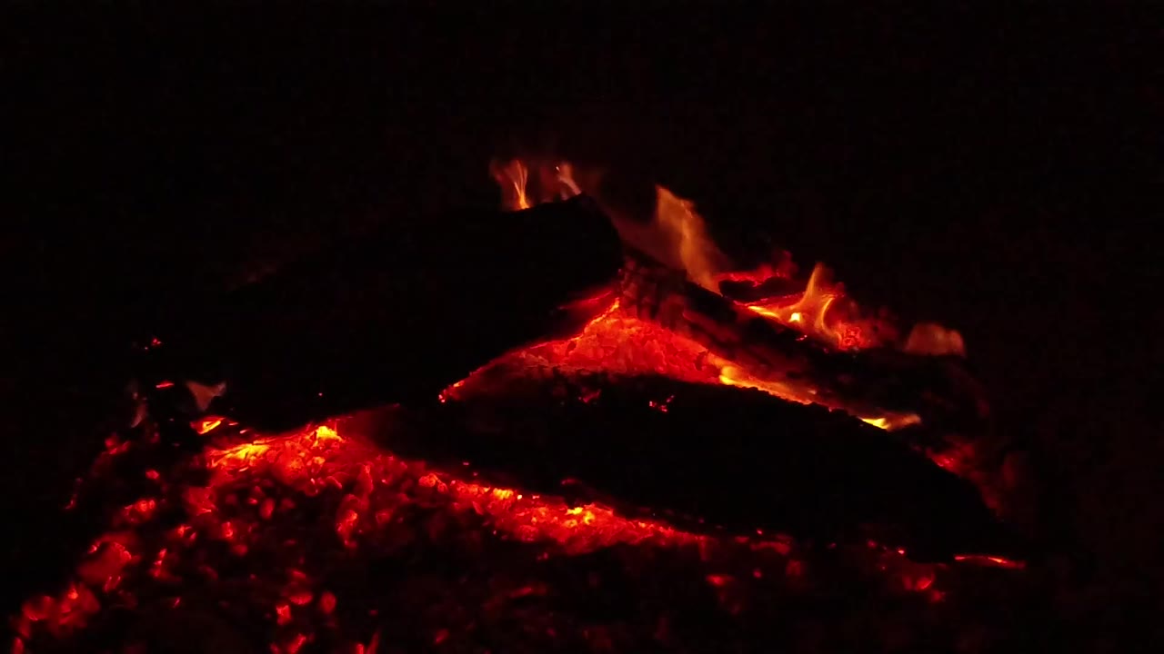 The Ojai campfire shows a dark log suspended over a red ember bed, with faint orange flame tracing the wood and no visible people.