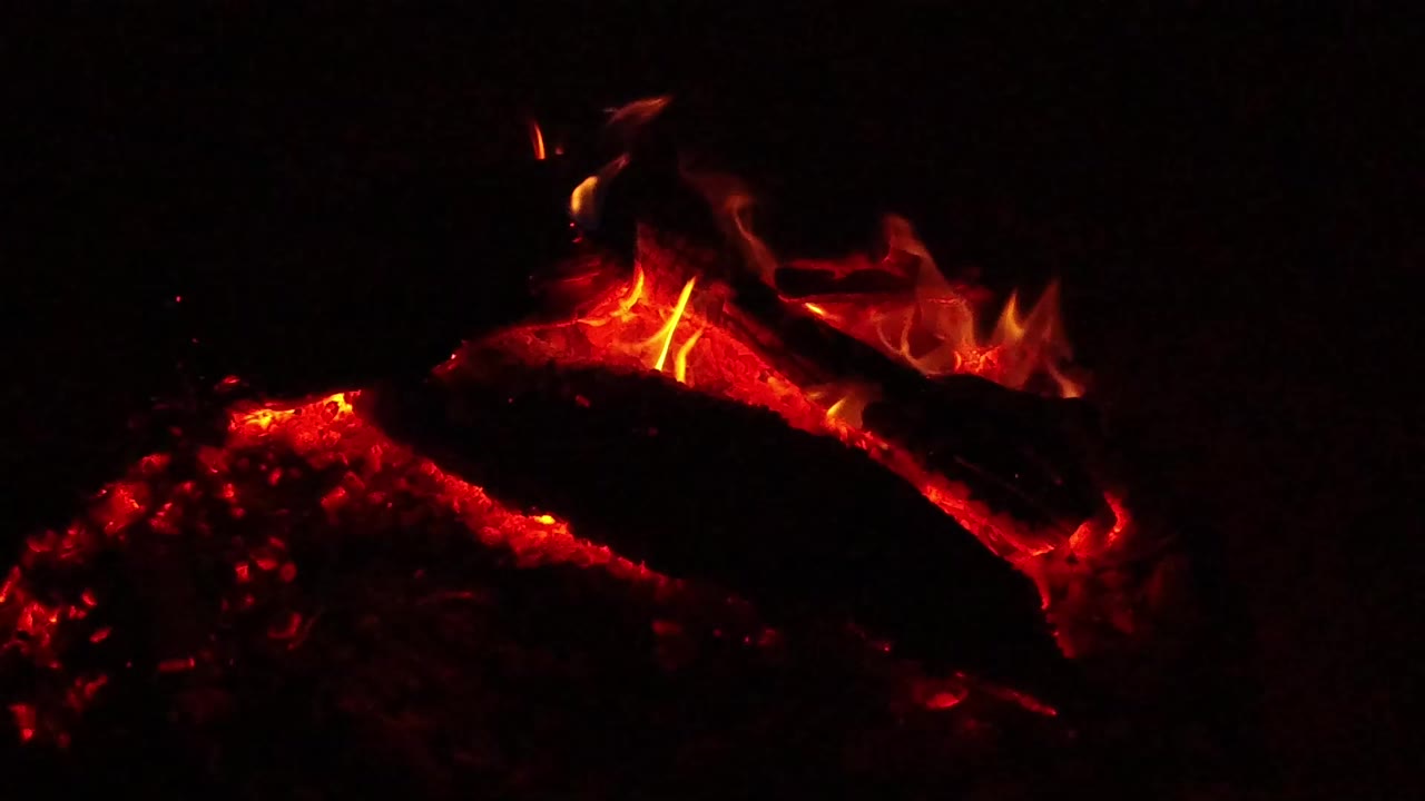 At 0:00, red hot coals and a charred burning log glow in Ojai, California, with small flame tips and no visible people.