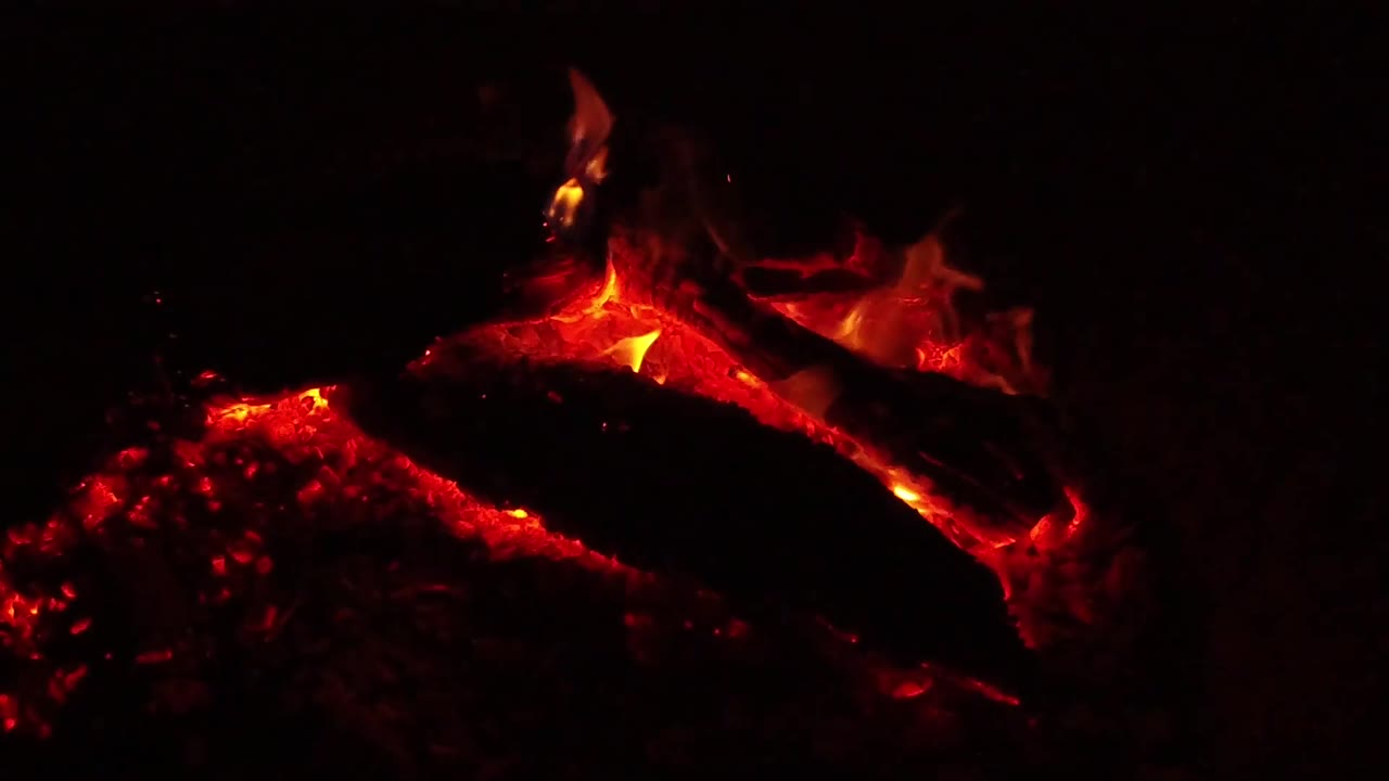 Bright flame flares above red coals and a log.