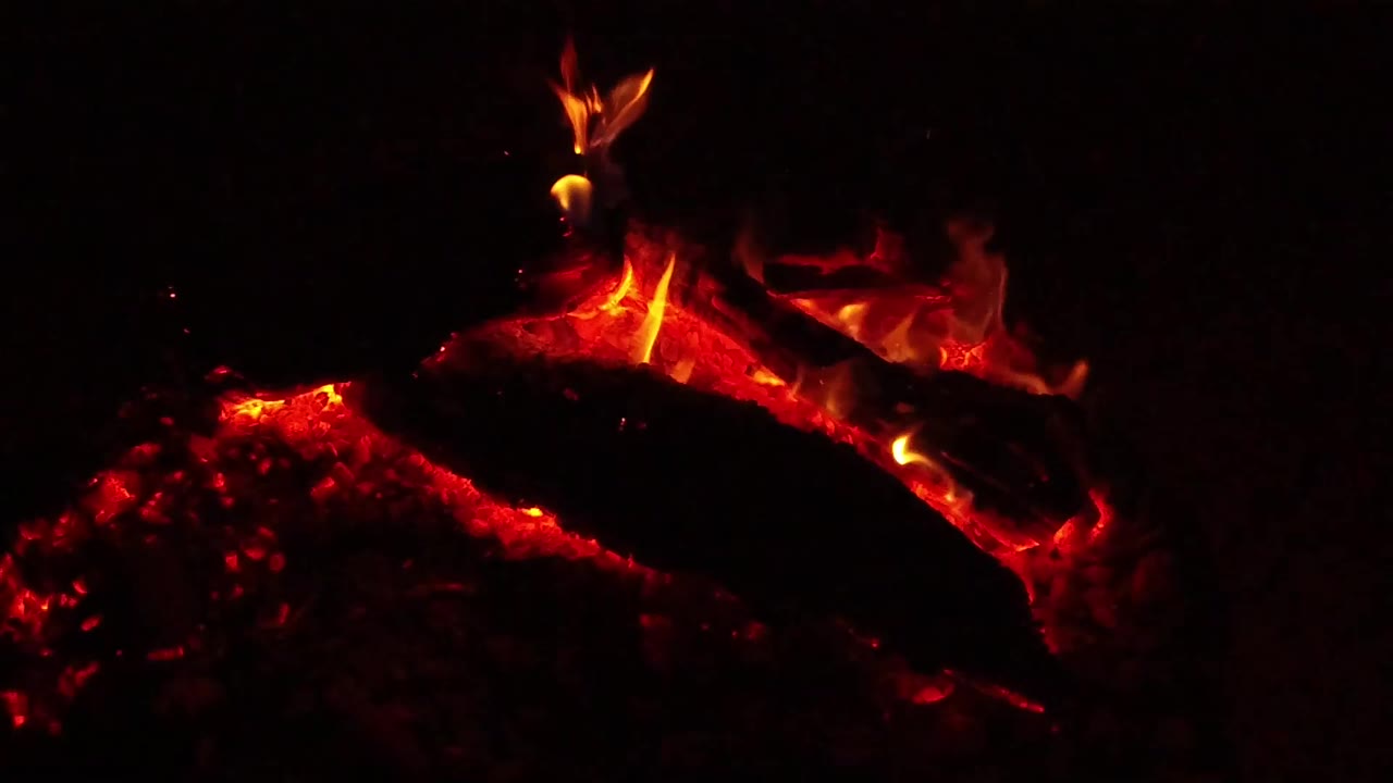 At 0:01, the Ojai fire close-up shows the coal bed glowing brighter below the log while a yellow-orange flame curls upward, with no visible people.