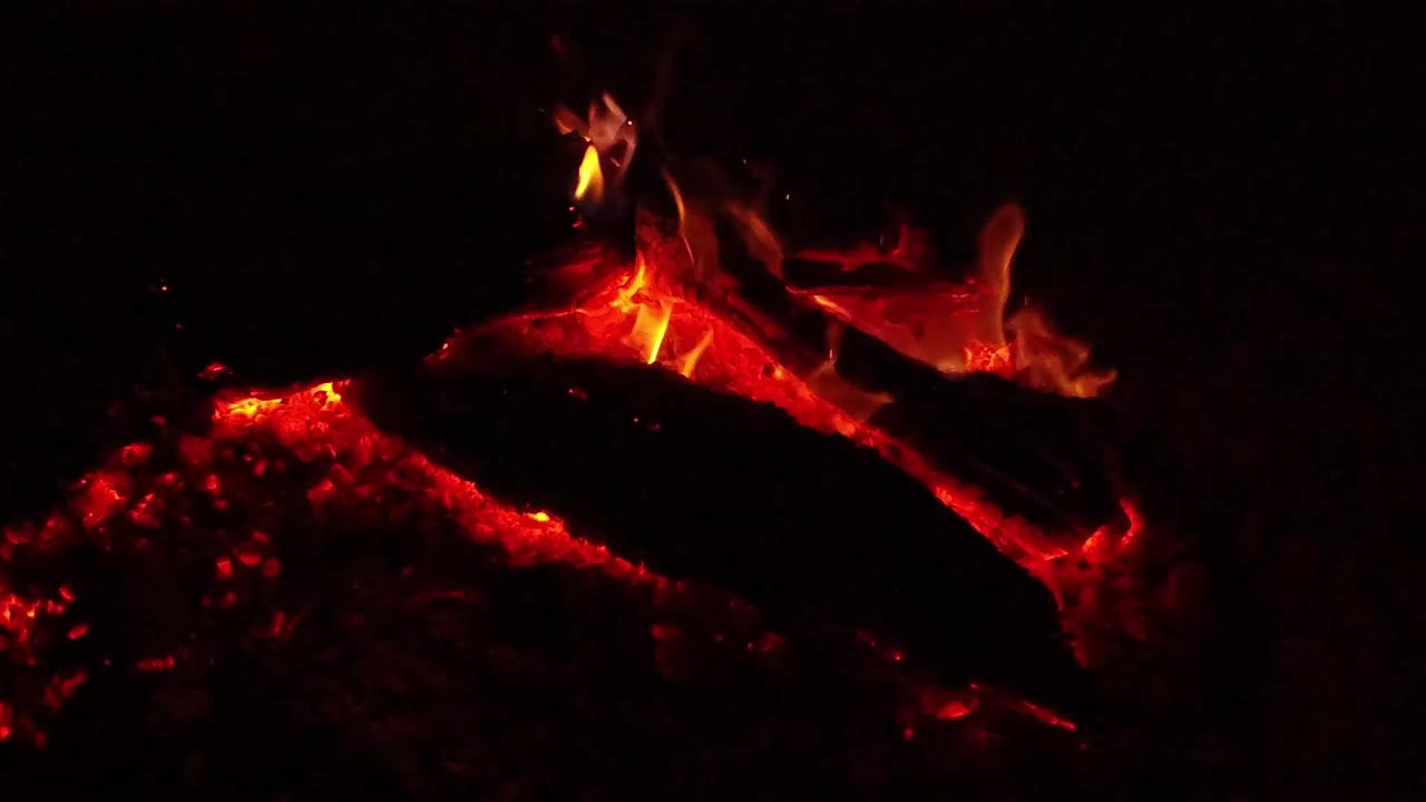 Glowing embers and a charred log with small flames in darkness.