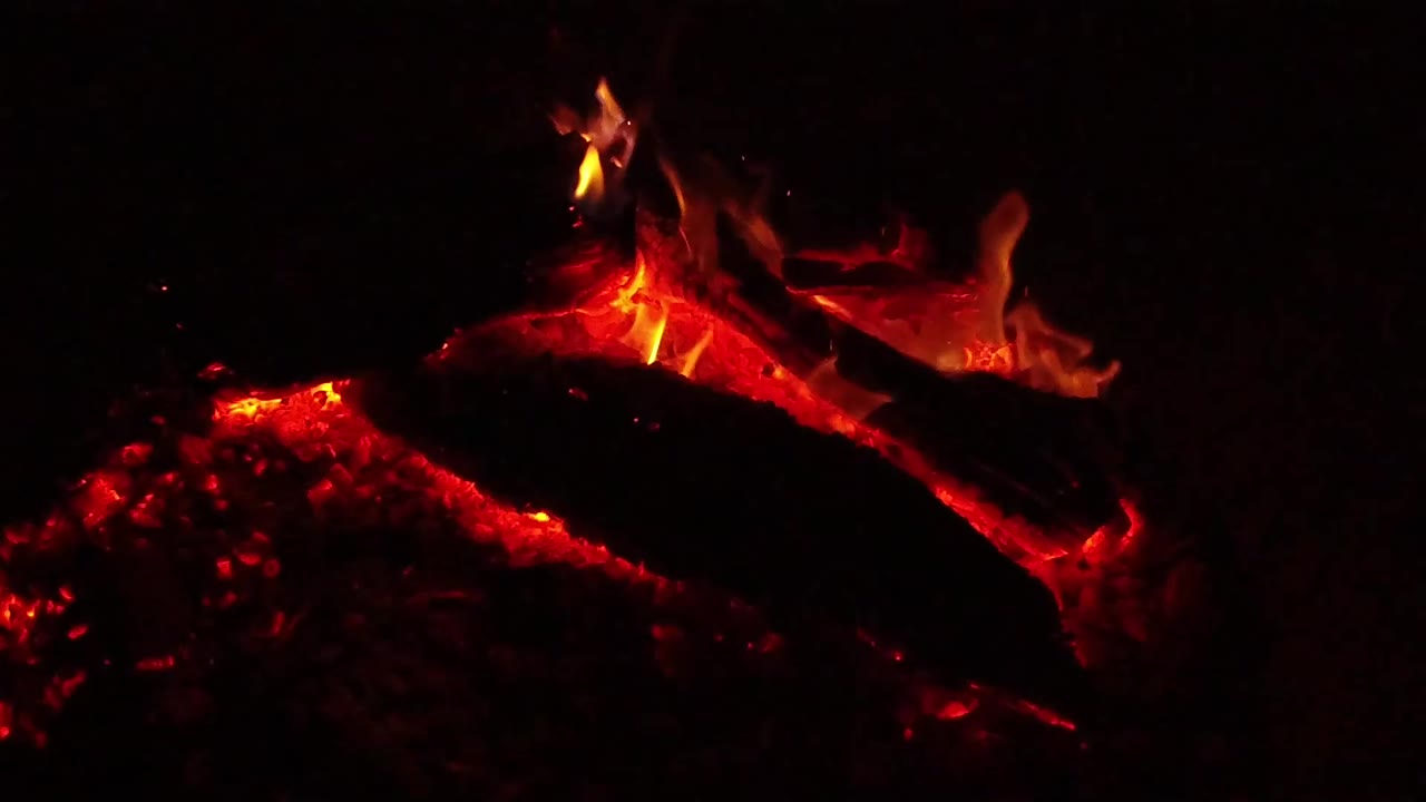 At 0:01 in Ojai, California, red coals glow under a diagonal blackened log while a brighter flame rises along the upper edge and no visible people appear.