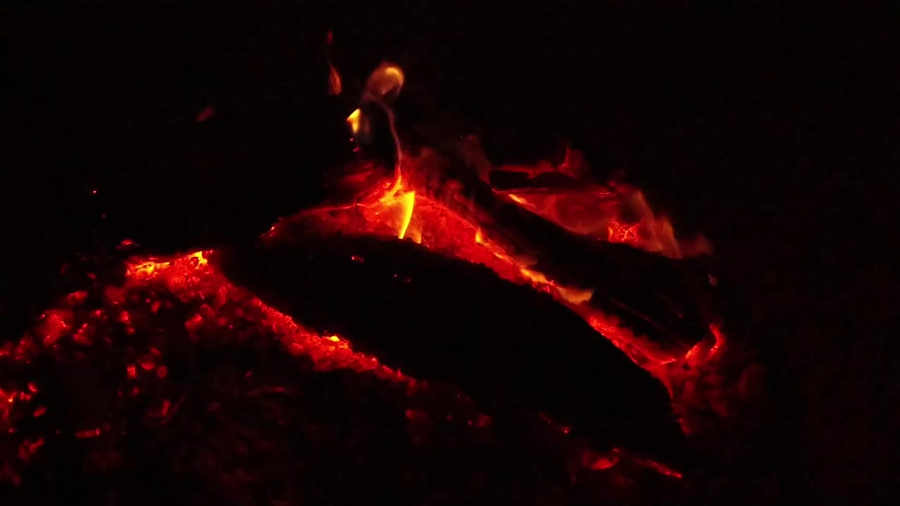 Red embers and a small yellow flame on a dark burning log.
