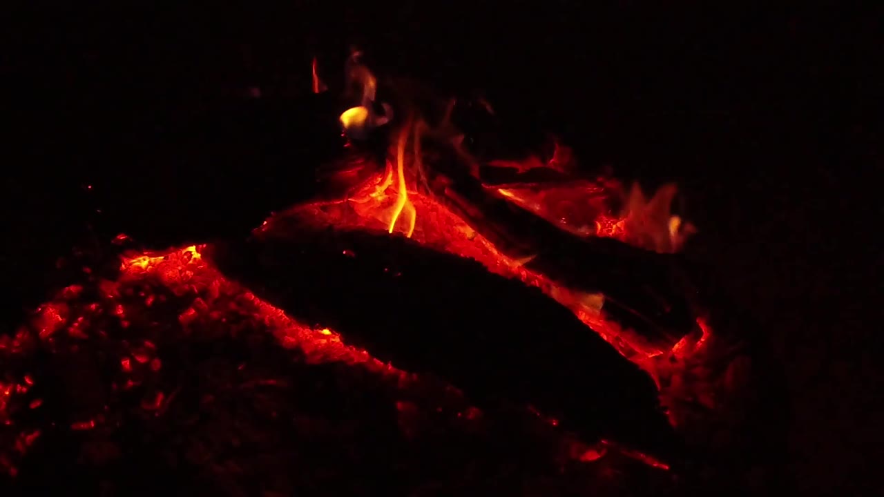 At 0:02, a small flame brightens near the top of the burning log while red-hot wood and coals glow beneath in Ojai, California, no visible people.