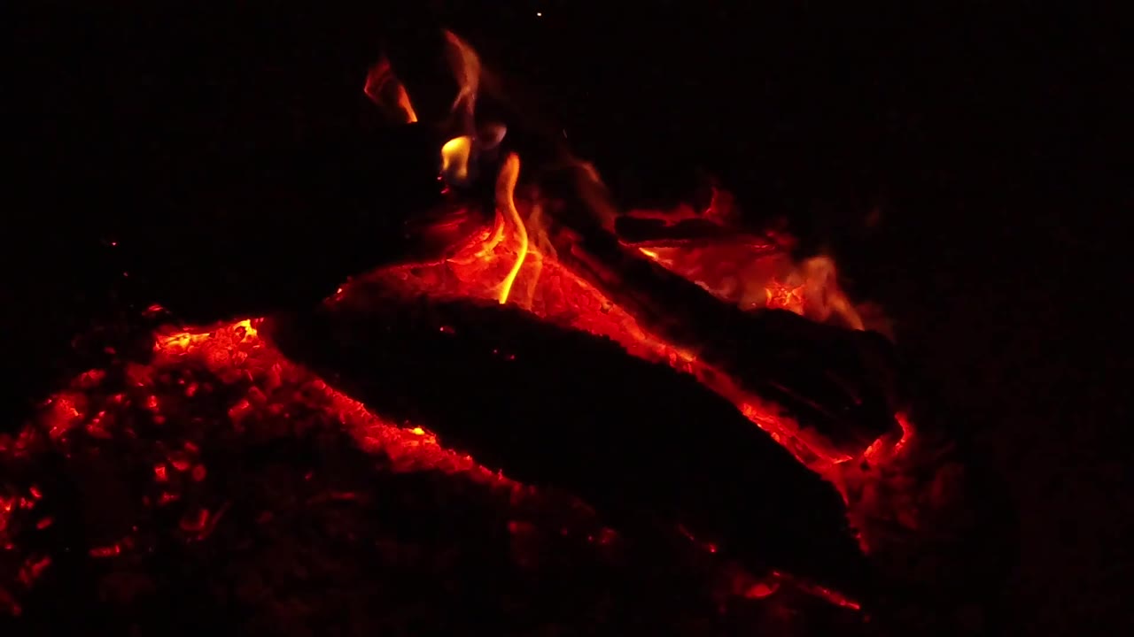 At 0:03, the Ojai, California campfire close-up shows a brighter yellow flame rising from the log with red ember light along the lower edge, no visible people.