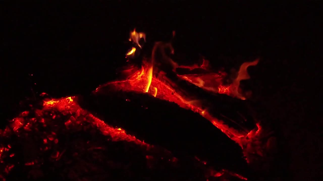At 0:02, a brighter flame curls above the burning wood while red embers remain clustered at left in Ojai, California, with no visible people.