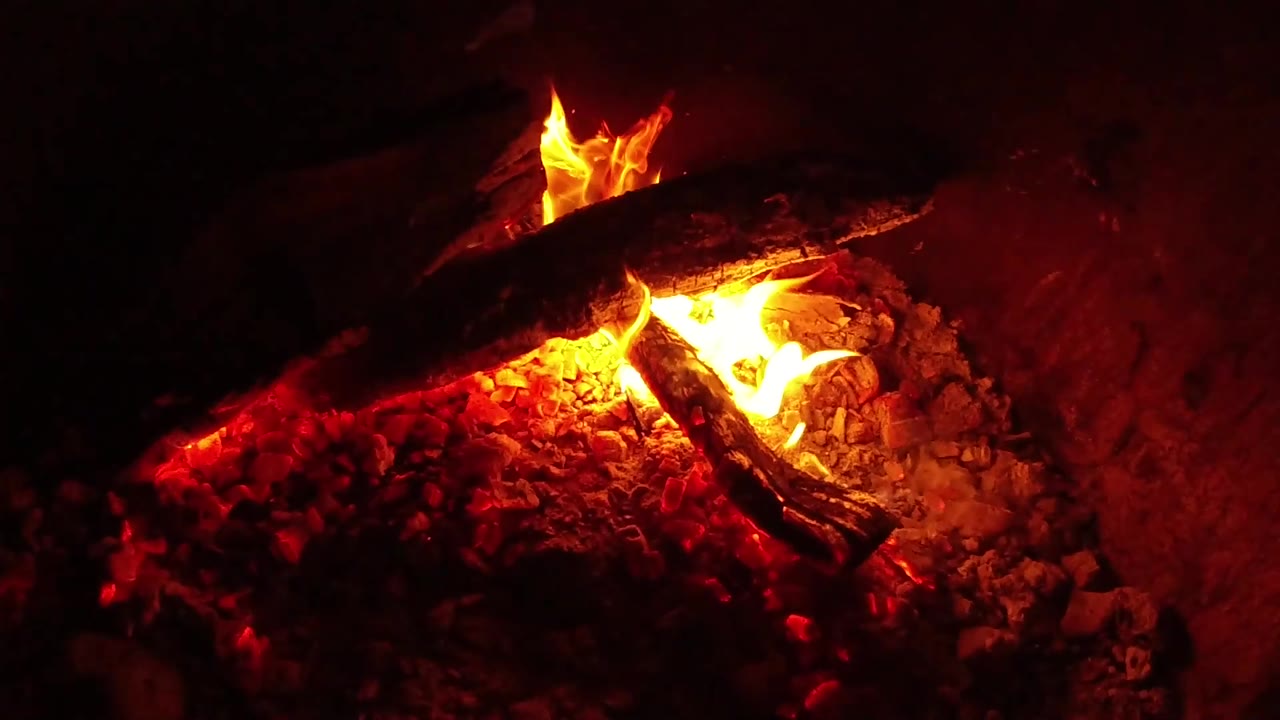 At 0:02, yellow flames flare wider across the glowing ember bed while a dark log spans the upper frame in Ojai, California, with no visible people.
