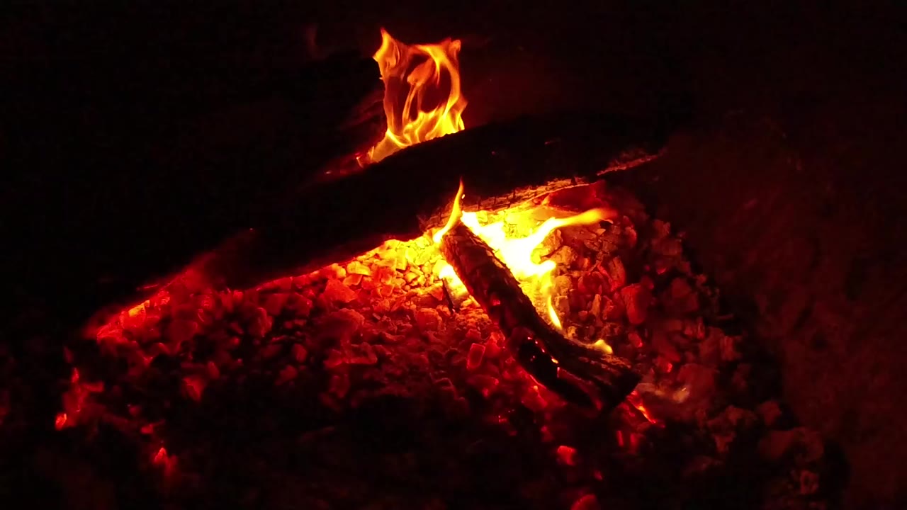 At 0:00, charred firewood lies over bright orange flames and red coals in Ojai, California, with no visible people.