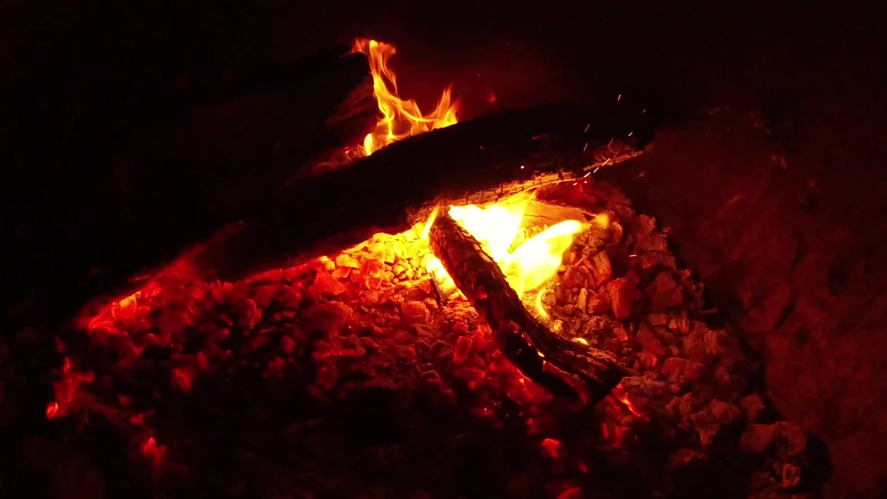 At 0:02, the fire burns brightest under the upper log, lighting the surrounding coals and blackened wood in Ojai, California, with no visible people.