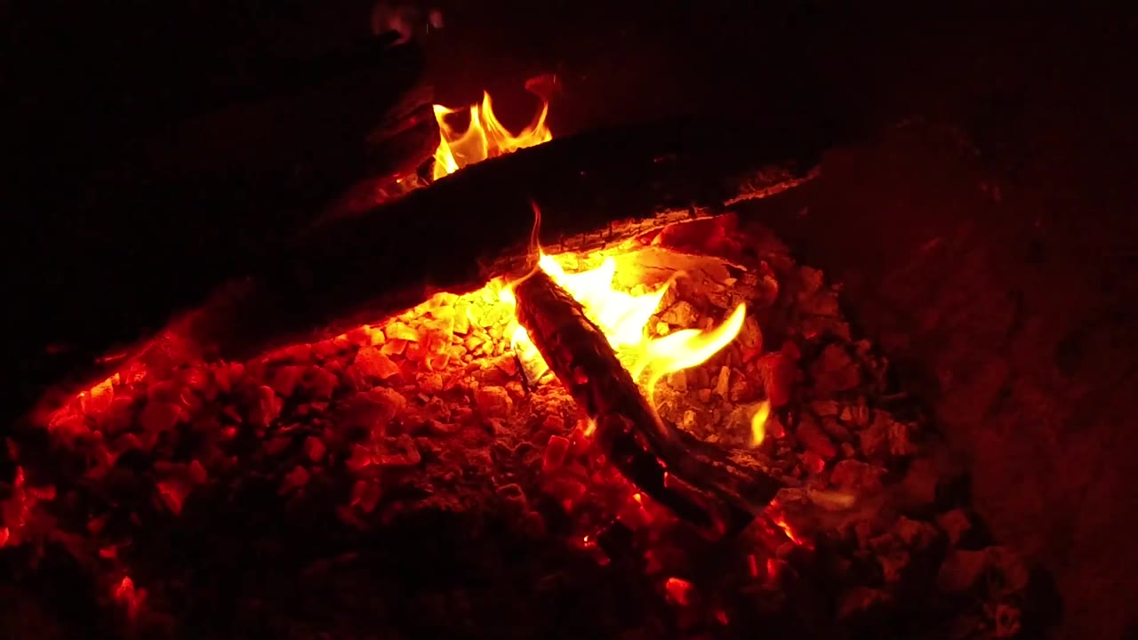 A curved yellow-orange flame wraps along the right side of the burning wood above red embers in Ojai, California, with no visible people.