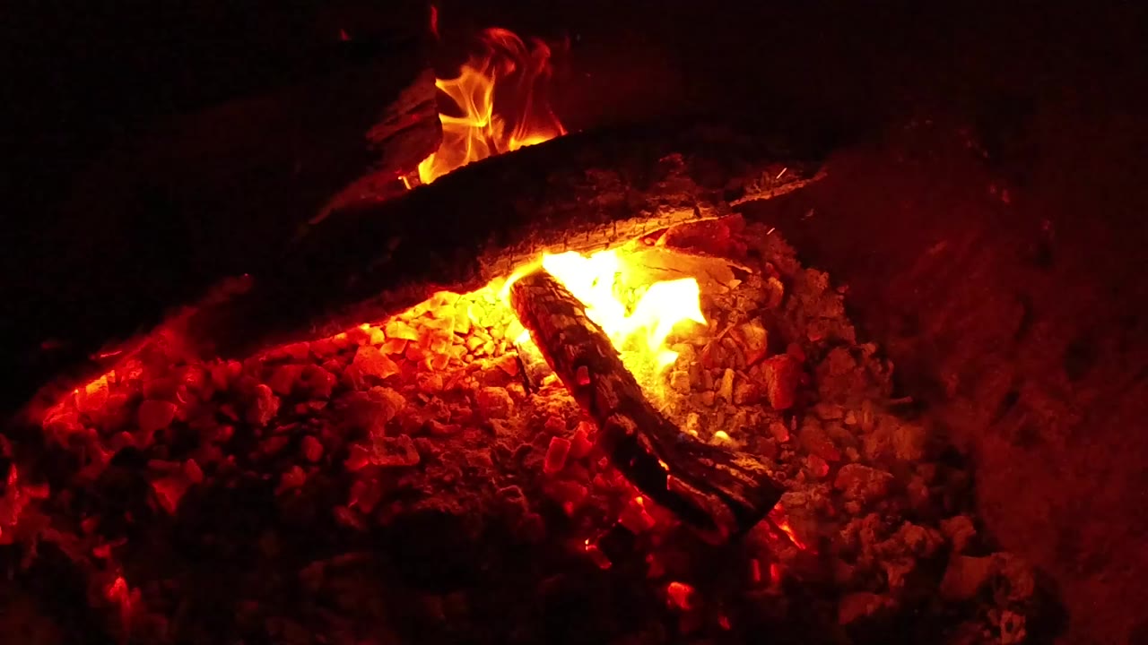 At 0:00, charred logs burn over red embers in a dark Ojai, California fire pit, with a bright flame near the center and no visible people.