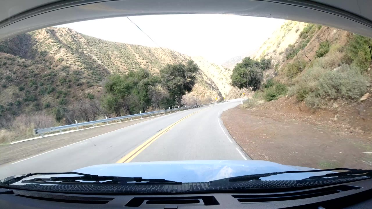 Front vehicle view of a two-lane road curving through dry hills near Ojai, California, with a guardrail, double yellow lines, and no visible people.