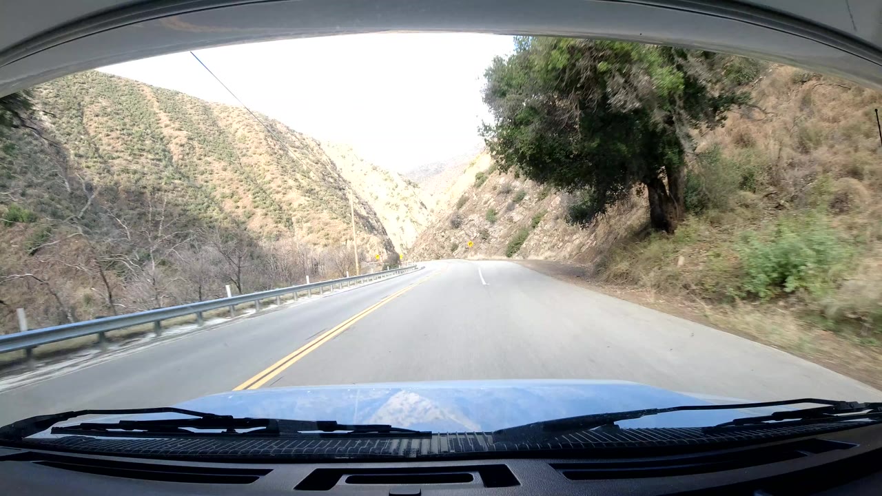 Two-lane road continuing between hillside and roadside guardrail