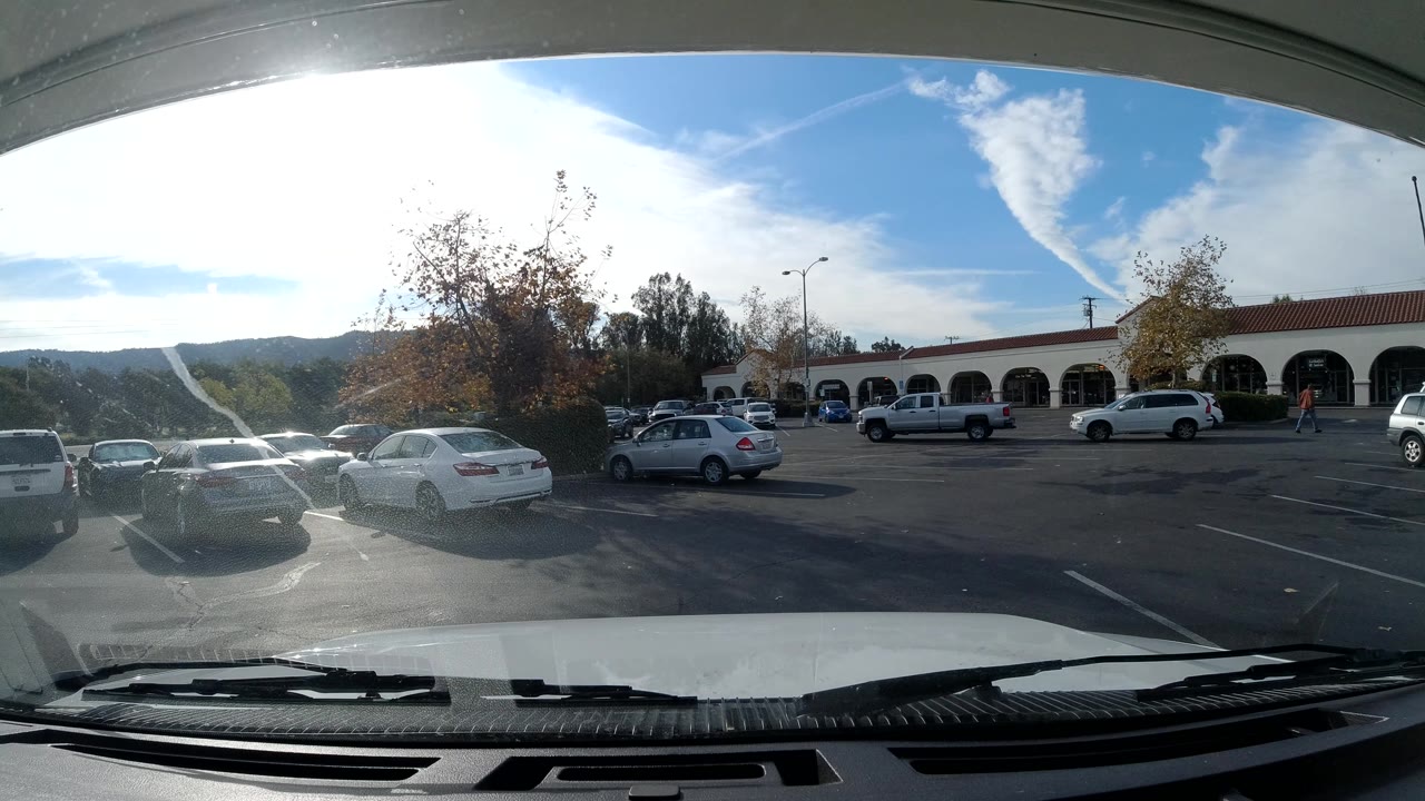 Parking lot foreground with cars and arched shopping center buildings in bright sunlight.