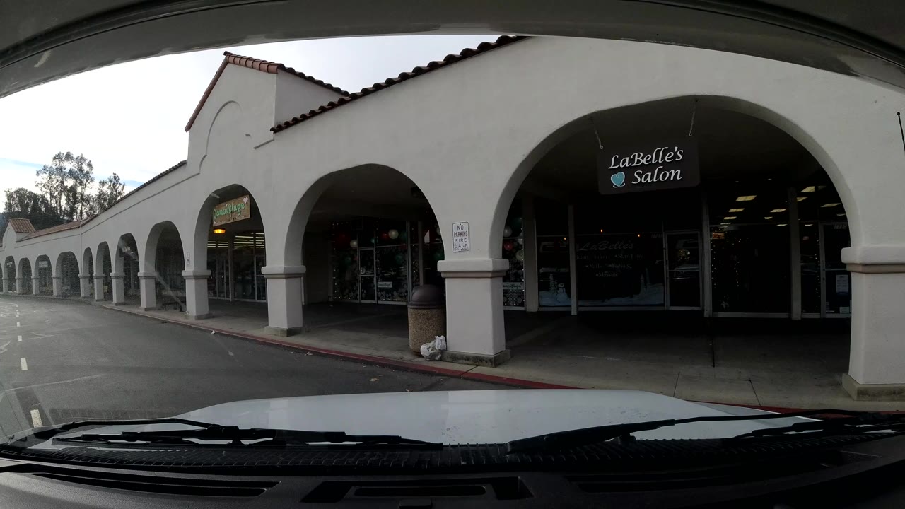 Close street-level view in Ojai, California of a shopping center arcade with a visible salon sign, parked cars, sidewalk, and no clearly visible people.