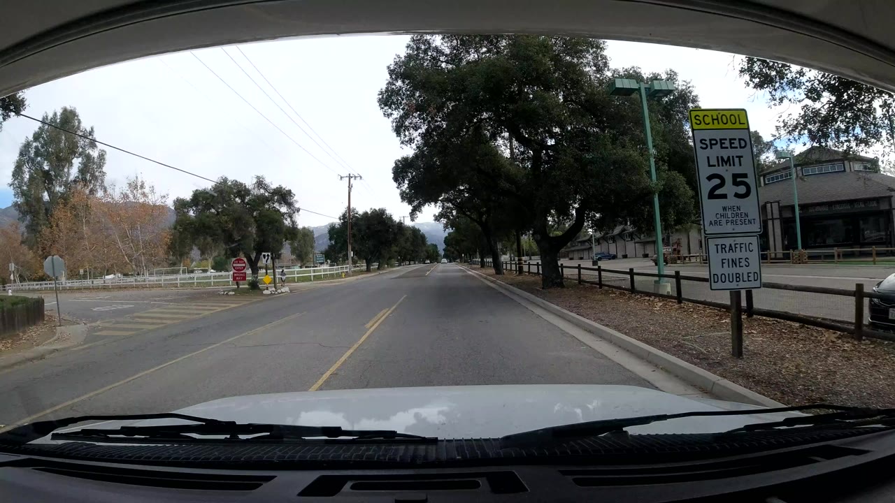 Two-lane road beside trees, fence, school speed limit sign, and buildings.