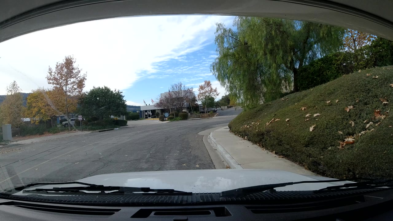 Interior car view in Ojai, California looking through the windshield at a quiet curving street, sidewalk, hedges, trees, and no visible people.