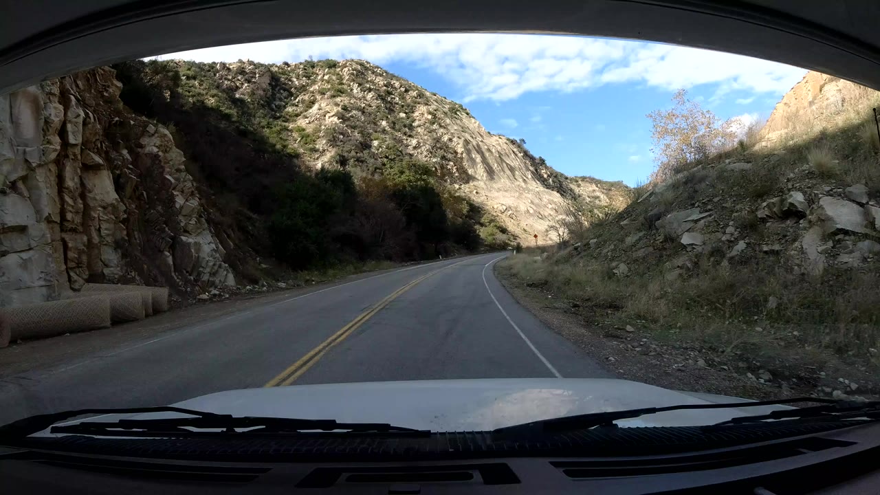Forward vehicle view on an Ojai, California mountain road curving left between rocky slopes, with dashboard edges visible and no visible people.