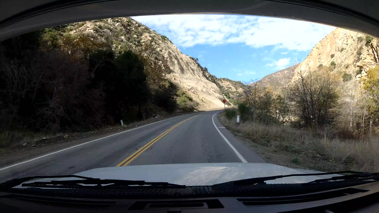 Vehicle POV farther along the Ojai road as the lane bends right, with brush and rock faces on both sides and no visible people.