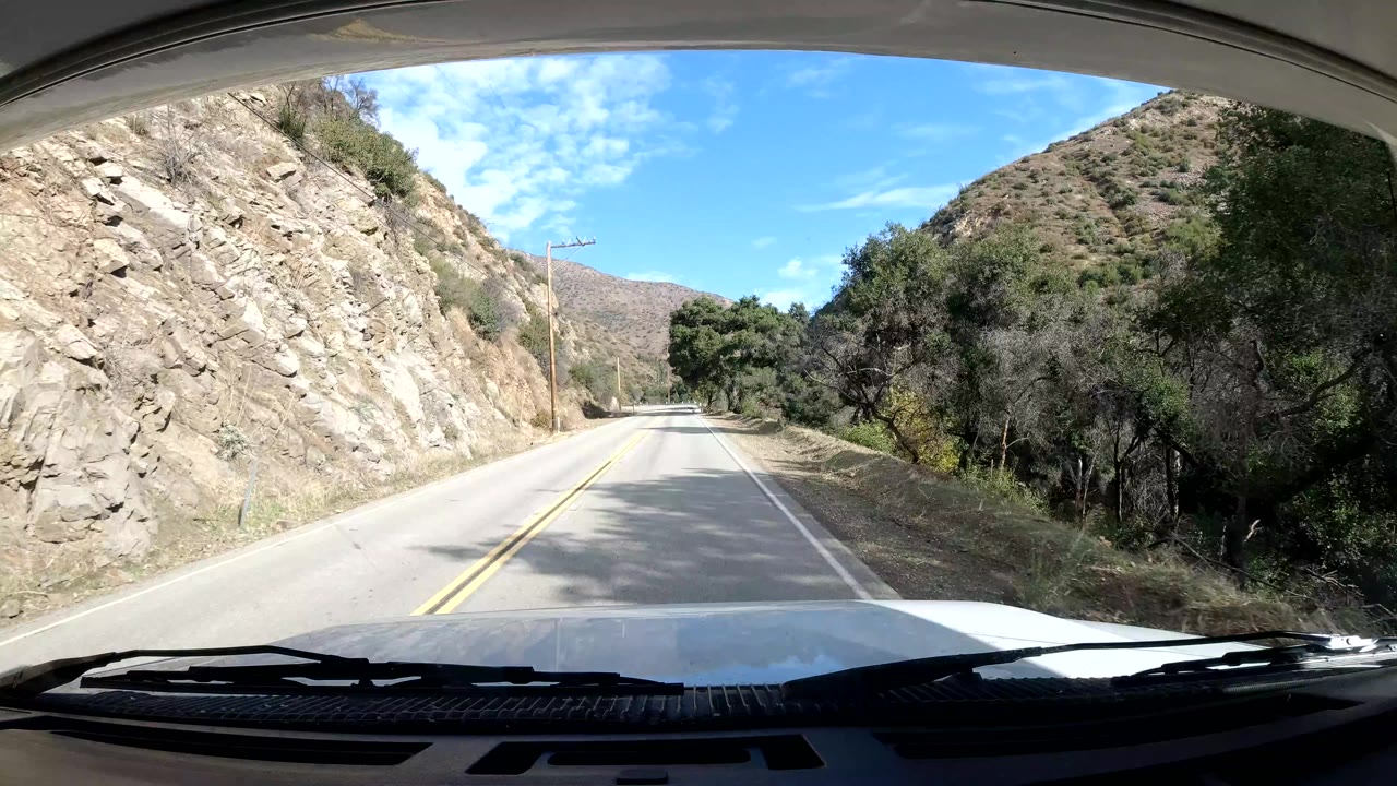 Straight two-lane road bordered by rock wall and trees.