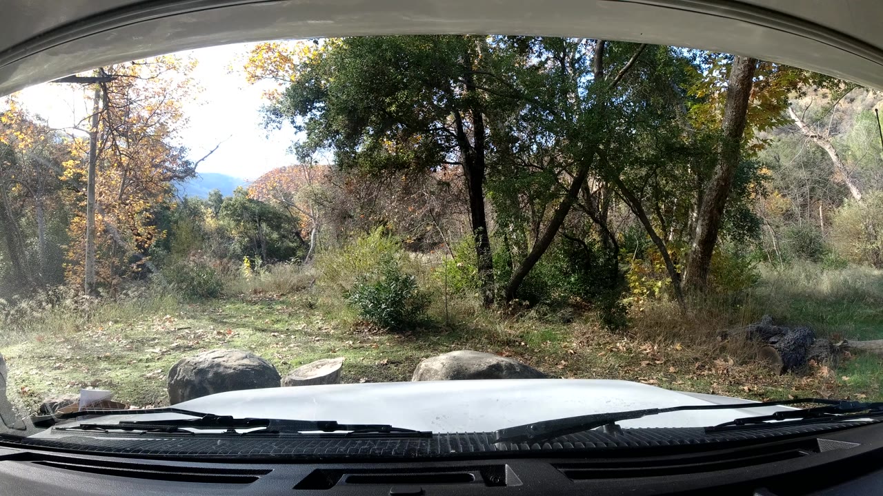 At three seconds, bright light catches the left side of the Ojai roadside view while the car hood, rocks, bushes, and tall trees stay in frame with no visible people.