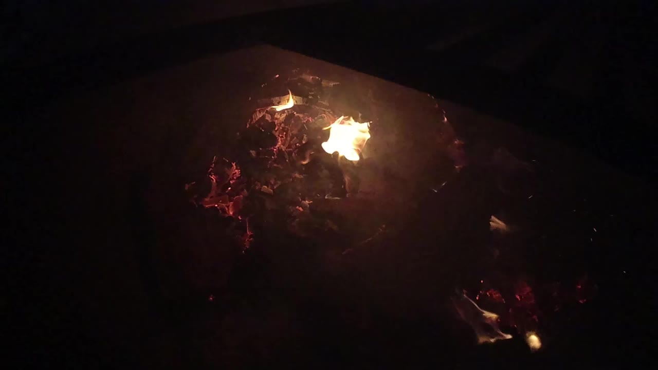 A small orange flame burns near the top of a dark bed of embers in Ojai, California, with black surroundings and no visible people.