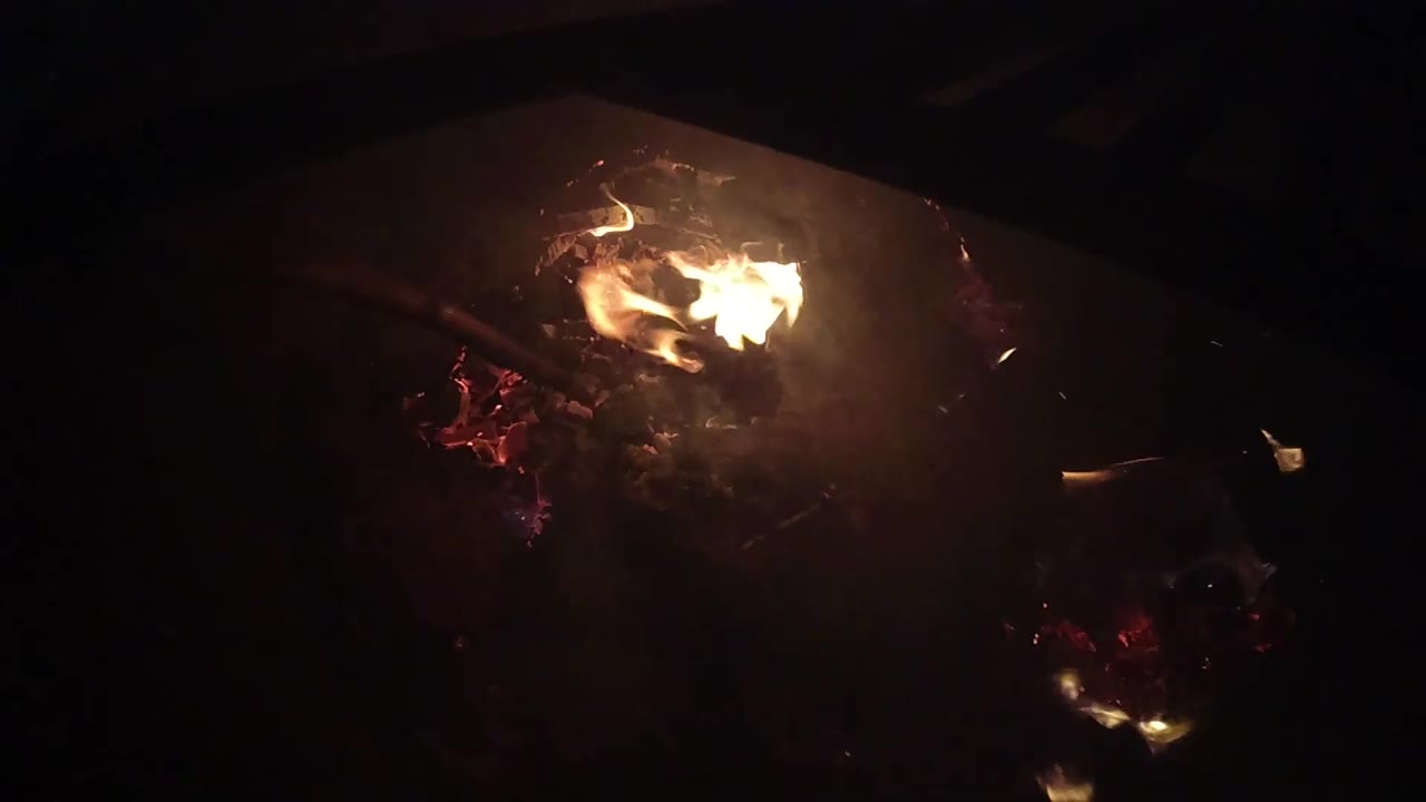 The flame curls across the ember pile in Ojai, California, with a few tiny sparks visible against the black background and no visible people.