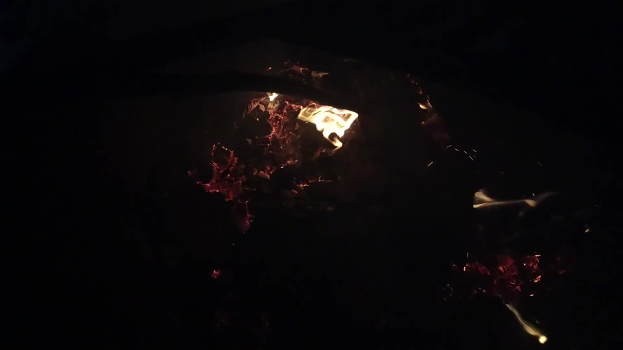 A triangular yellow flame leans over glowing red embers in the dark Ojai campfire frame, with no visible people.
