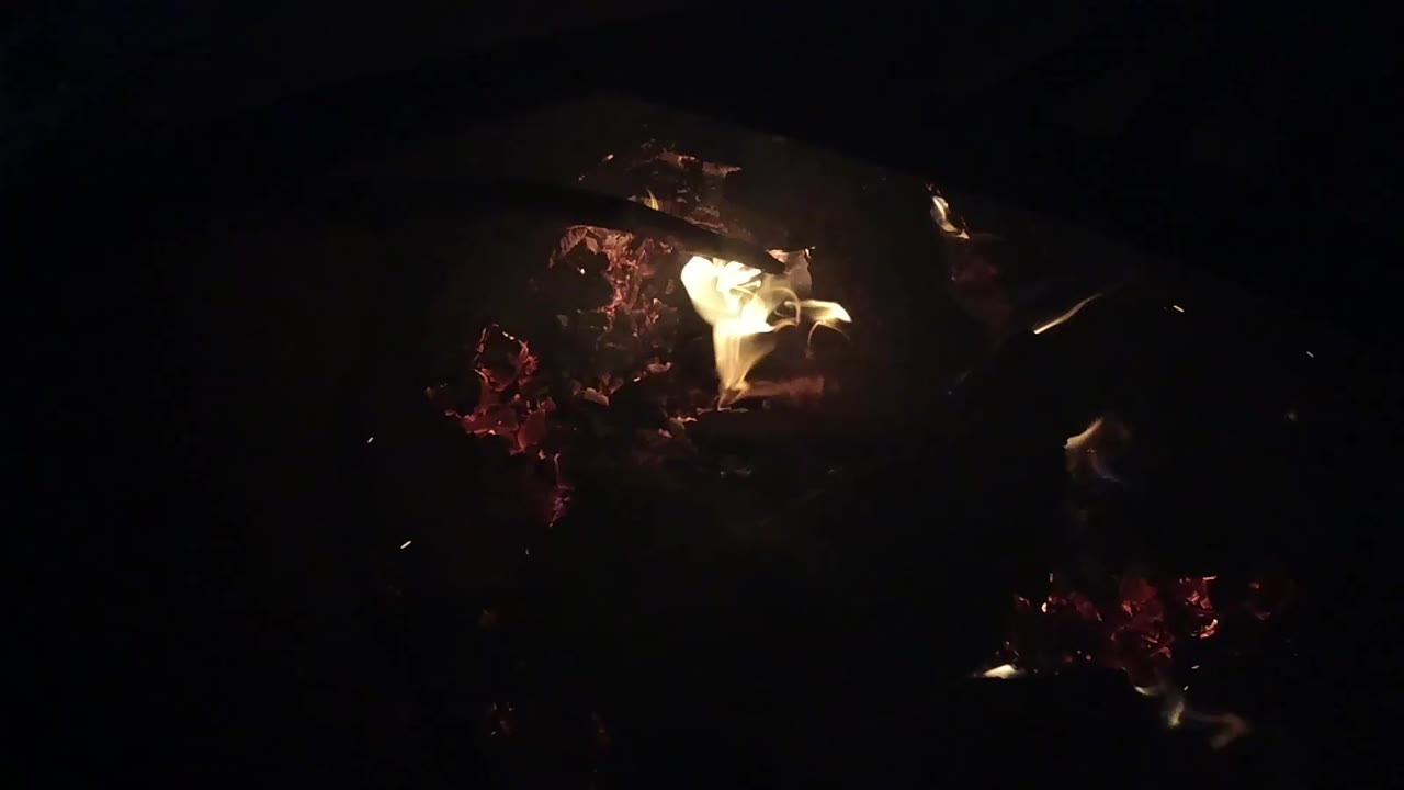 At 0:01, the flame brightens near the upper center of the dark campfire logs in Ojai, California, with no visible people.