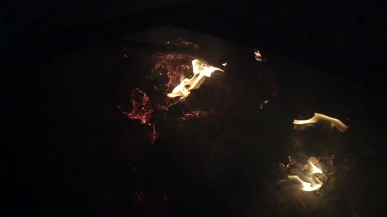 At the start of the Ojai clip, small yellow flames burn over red embers in a mostly black frame with no clearly visible people.