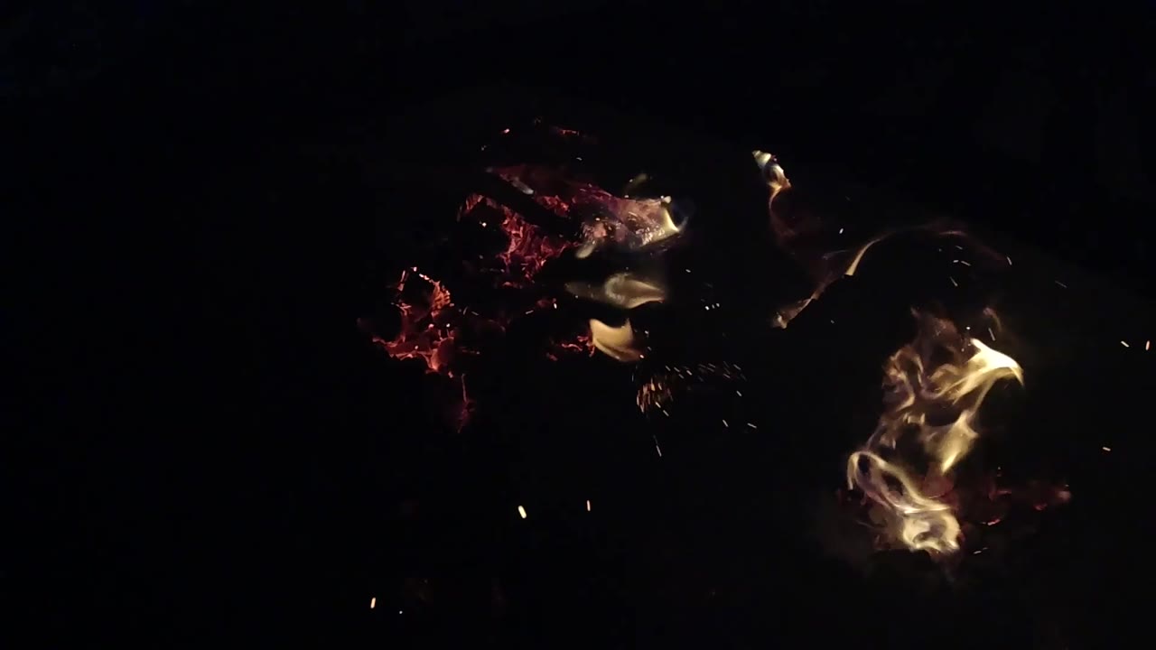 Curled flames flare around red embers while small sparks scatter through the darkness in Ojai, California, with no visible people.