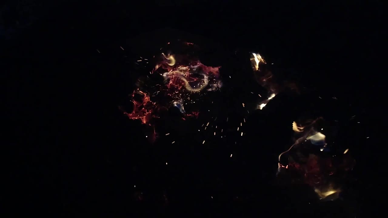 At 0:03, red embers and pale flame sit left of center while a spray of bright sparks appears lower right against the black background, with no visible people.