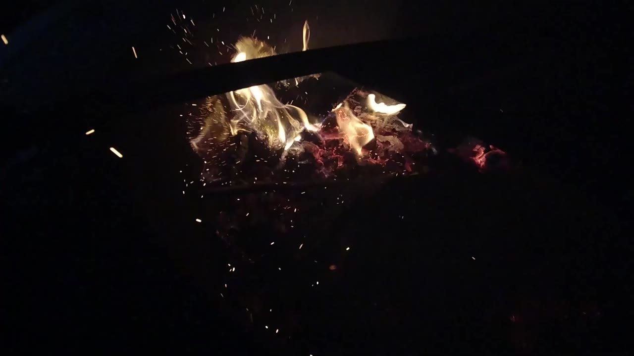 Close flames burn over red embers in Ojai, California, with small sparks rising into a mostly black frame and no visible people.