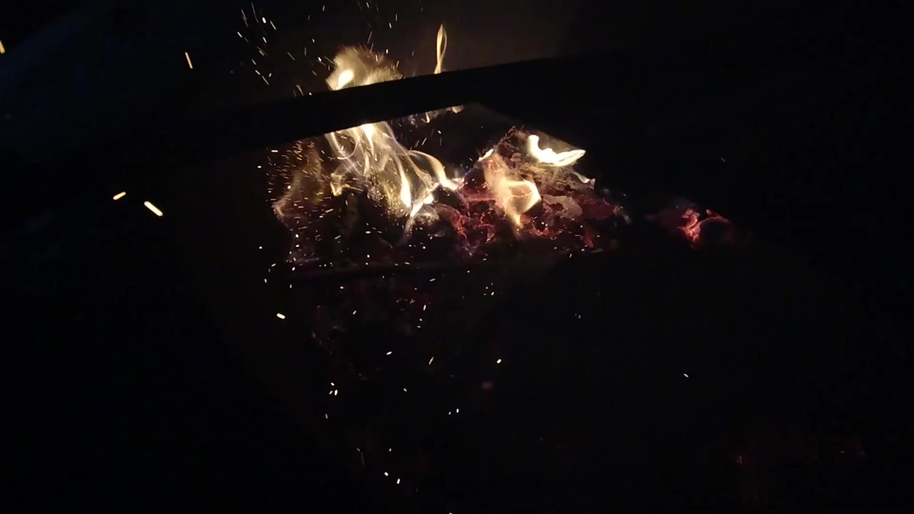 Bright flames curl above glowing coals with sparks nearby.