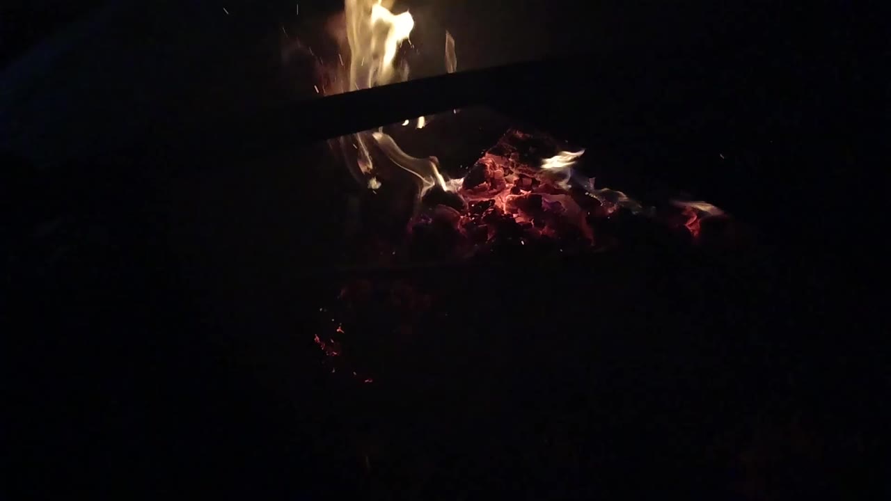 Small flames rising from red embers in darkness