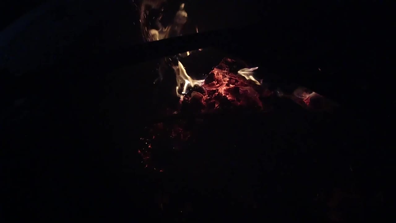 At 0:02, dim flames lean over a red ember bed in Ojai, California, with a dark diagonal edge cutting across the top and no visible people.