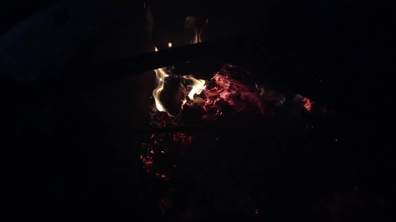At 0:02, a compact flame rises near the left side of the ember bed in Ojai, California, with the background almost entirely dark and no visible people.
