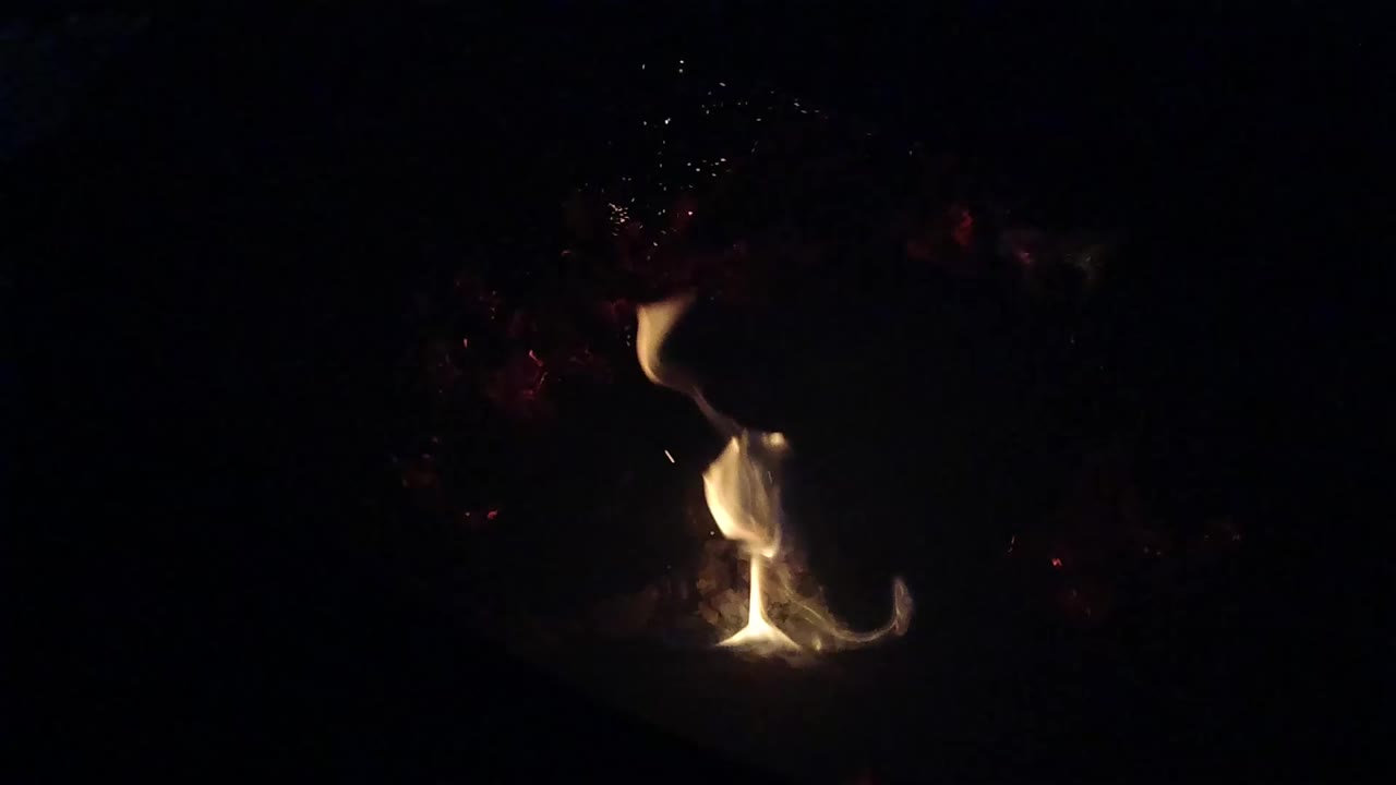 Small flame glowing in a dark fire pit