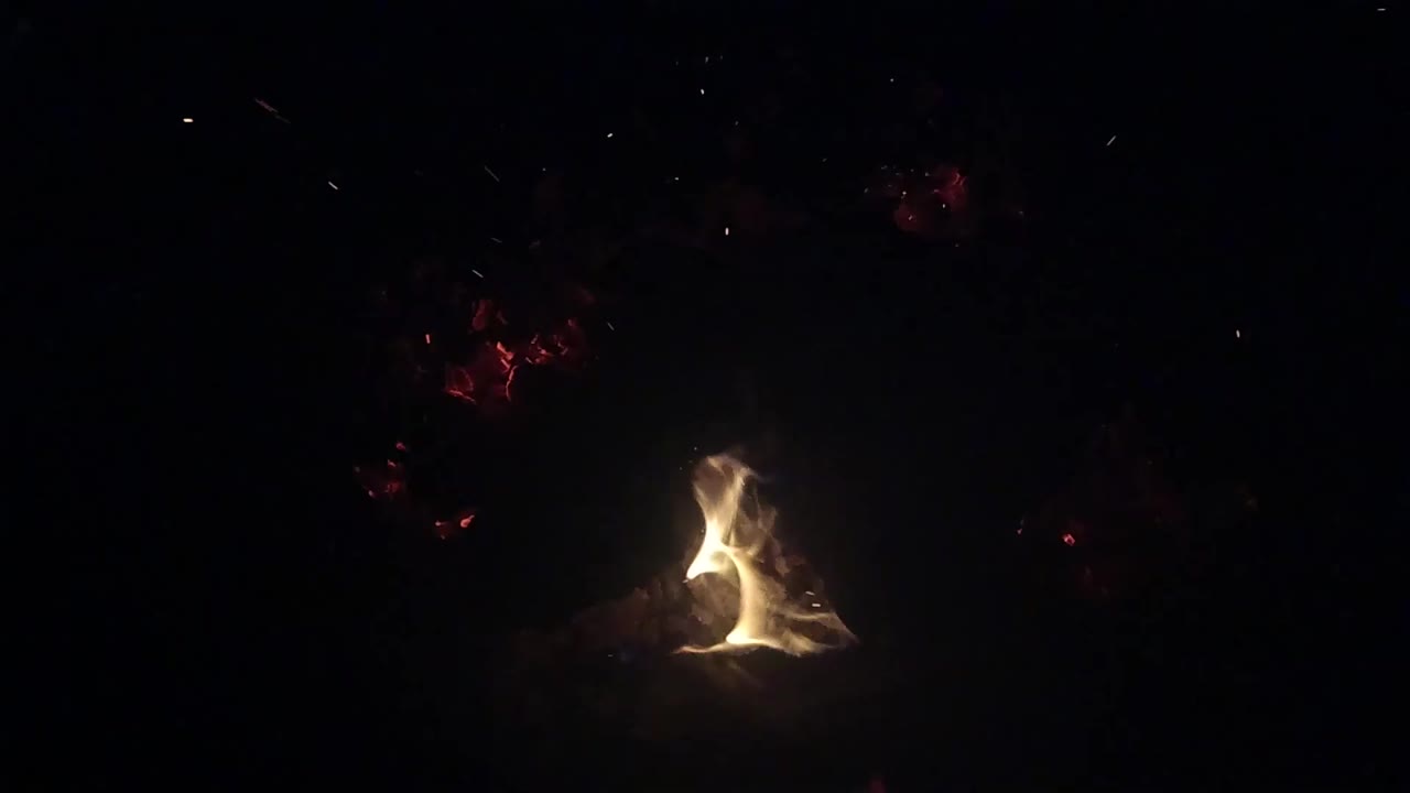 Bright flame rising from a small fire in a dark scene.