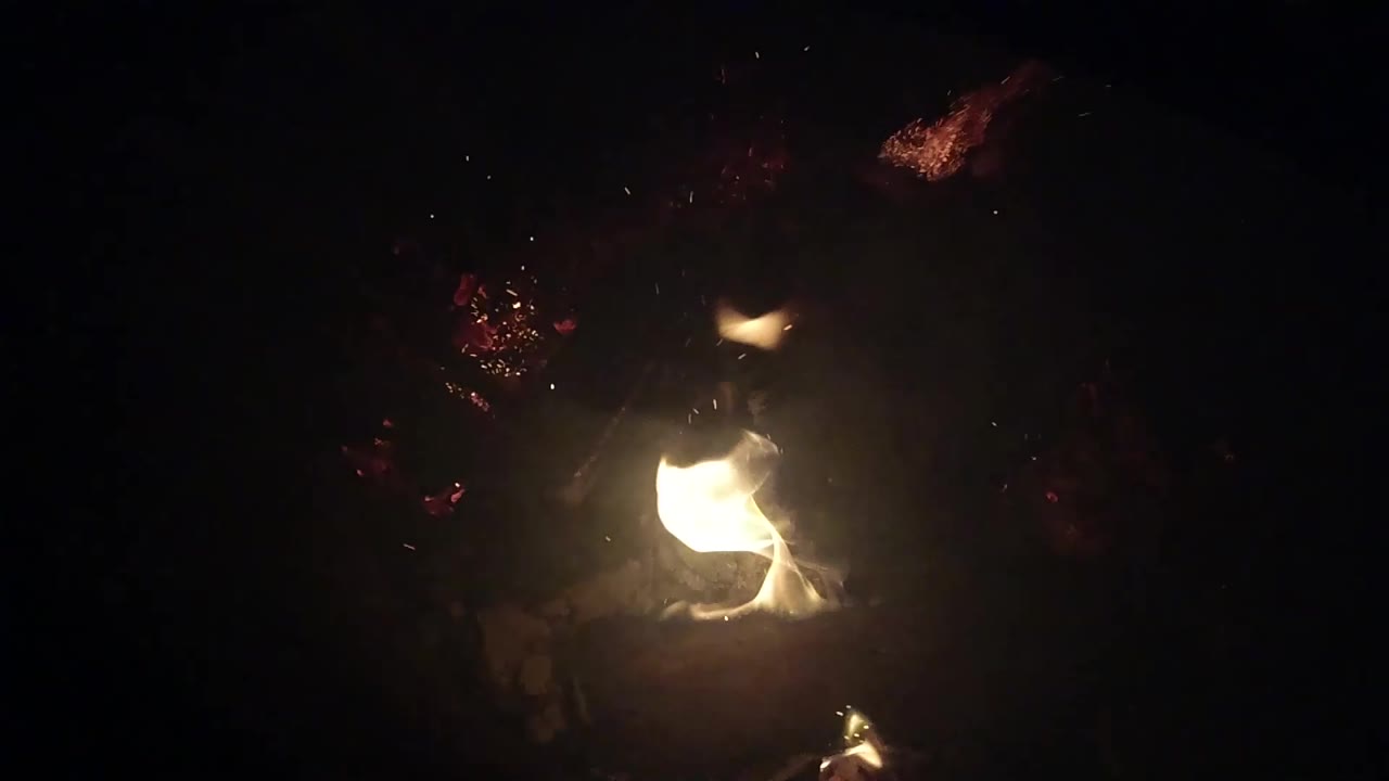 A compact flame glows beside dark leaves and scattered embers in Ojai, California, with no visible people in the shot.