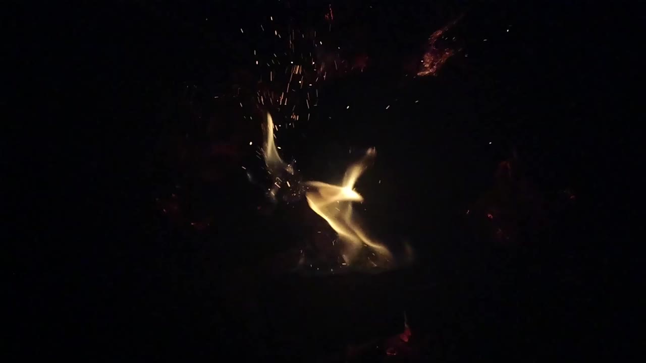 A brighter tongue of fire leans across the lower center of the Ojai, California frame while tiny sparks rise into darkness and no people are visible.