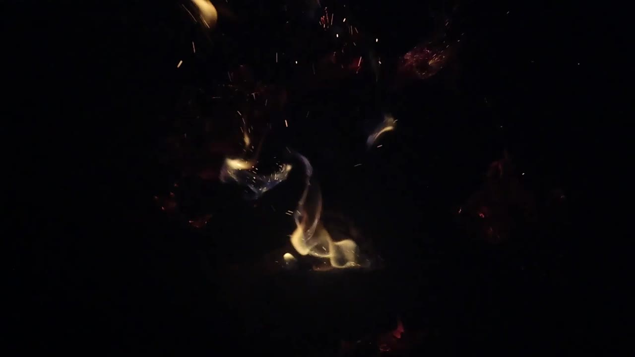 A low yellow flame burns near the bottom of the Ojai, California frame under faint red ember patches and drifting sparks, with no visible people.
