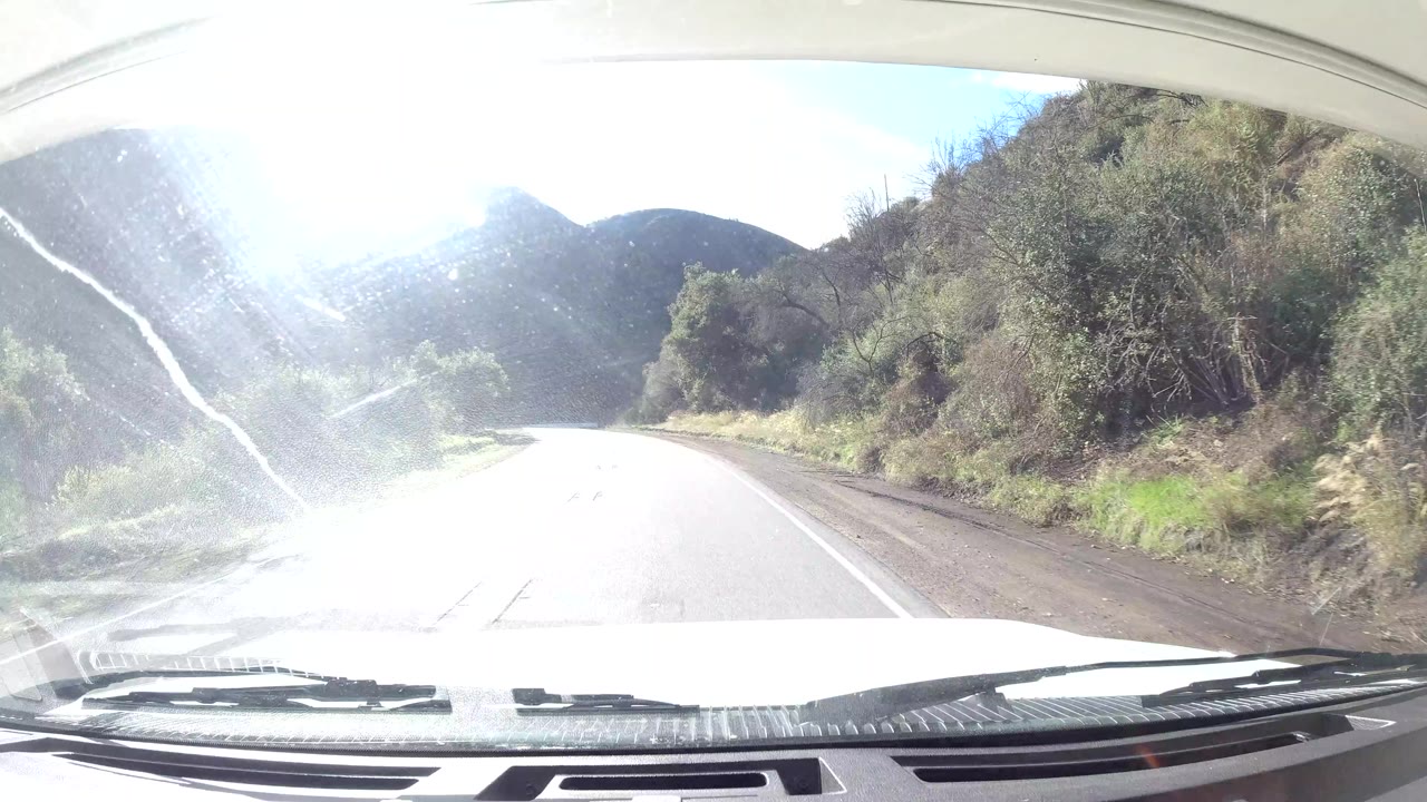 Second frame shows the Ojai, California road continuing around a bright bend, with heavy windshield reflection, roadside brush, and no visible people.