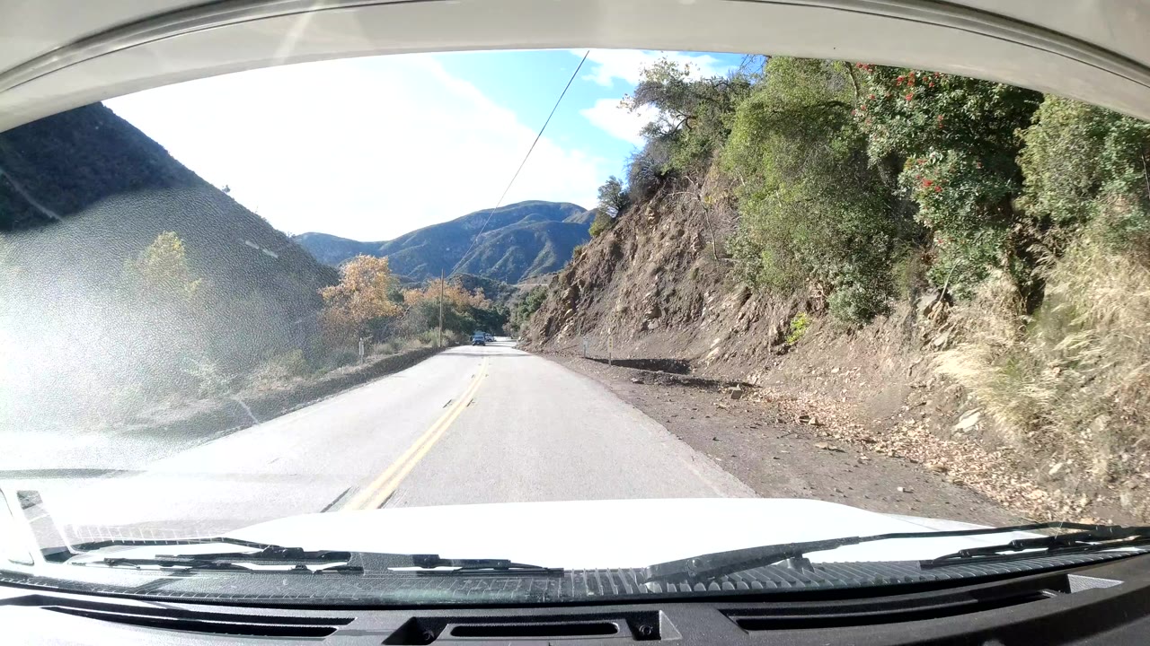 Third frame shows the car progressing along an empty Ojai, California mountain road, with a rocky cut slope on the right, brush on both sides, and no visible people.